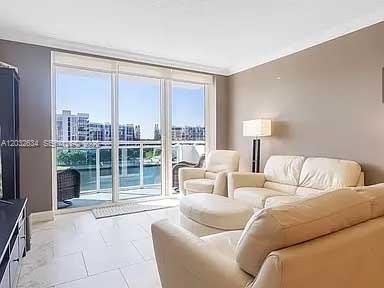 A living room with white tile floors, a beige sofa, and a balcony overlooking water — 3000 S Ocean Dr # 420, Hollywood FL 33019, HOLLYWOOD, FL