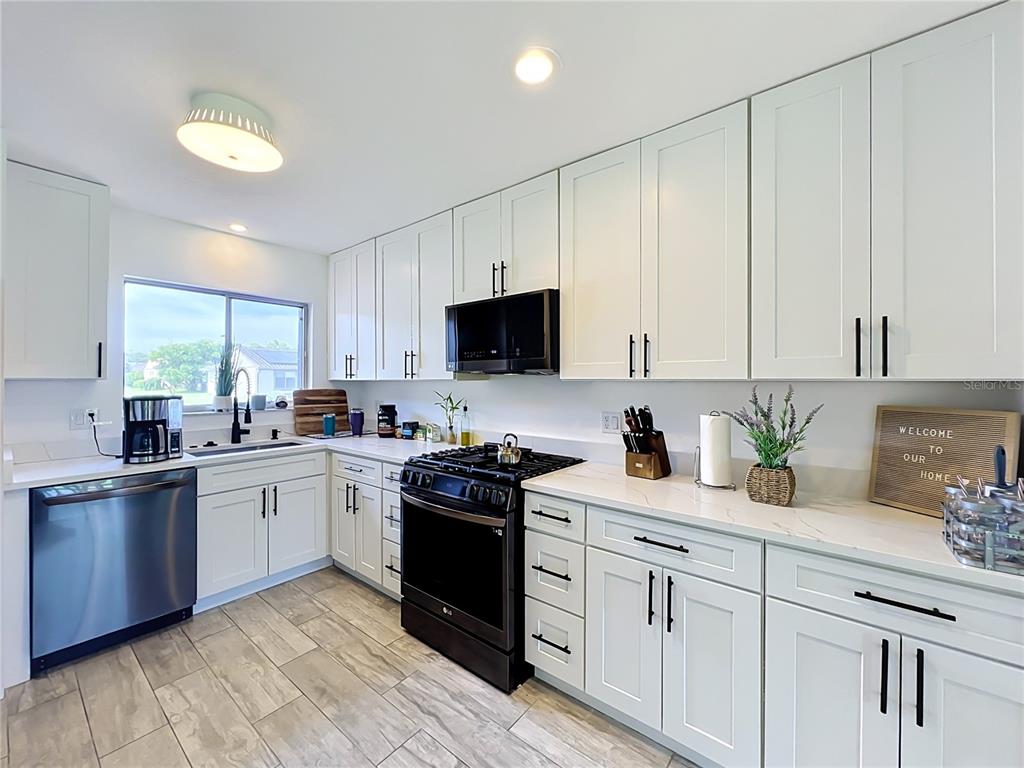 A kitchen features white shaker cabinets, stainless steel appliances, and light wood-look tile flooring — 5501 MEMORIAL DRIVE, ORLANDO, FL