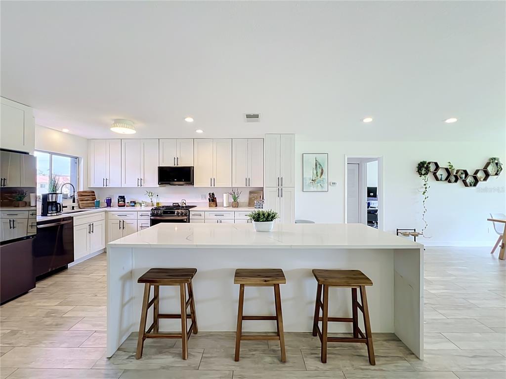 A modern kitchen features white cabinetry, a large waterfall island with three stools, and tile flooring — 5501 MEMORIAL DRIVE, ORLANDO, FL