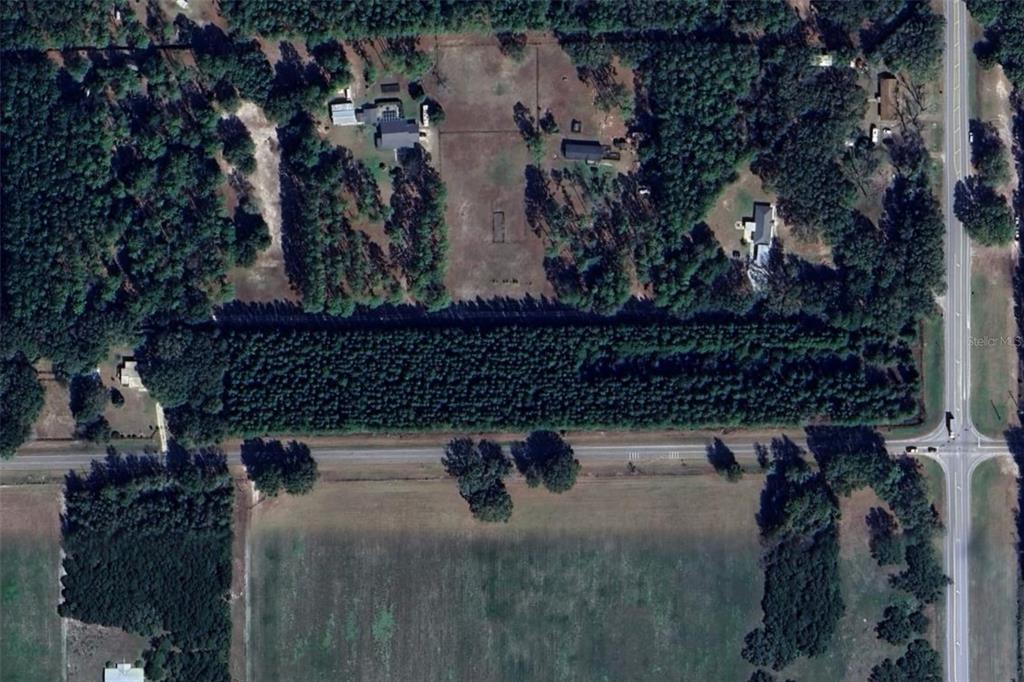 An aerial view shows a large, wooded property divided by a road with nearby houses — 7818 NW STATE ROAD 45, HIGH SPRINGS, FL
