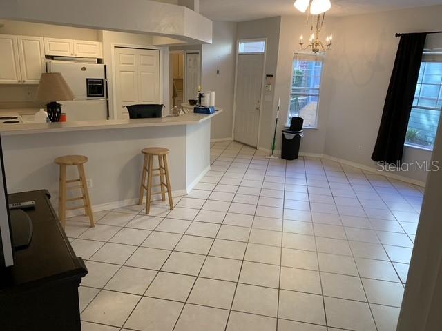A kitchen with a breakfast bar, two stools, and white tile flooring opens to a room — 350 NW 50 BOULEVARD UNIT 350, GAINESVILLE, FL