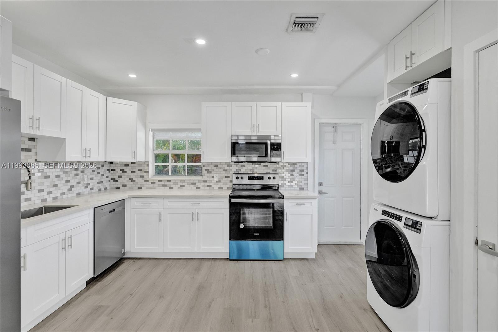 A modern kitchen features white cabinetry, stainless steel appliances, a tiled backsplash, and stacked laundry — 4326 NW 4th St, Miami FL 33126, MIAMI, FL