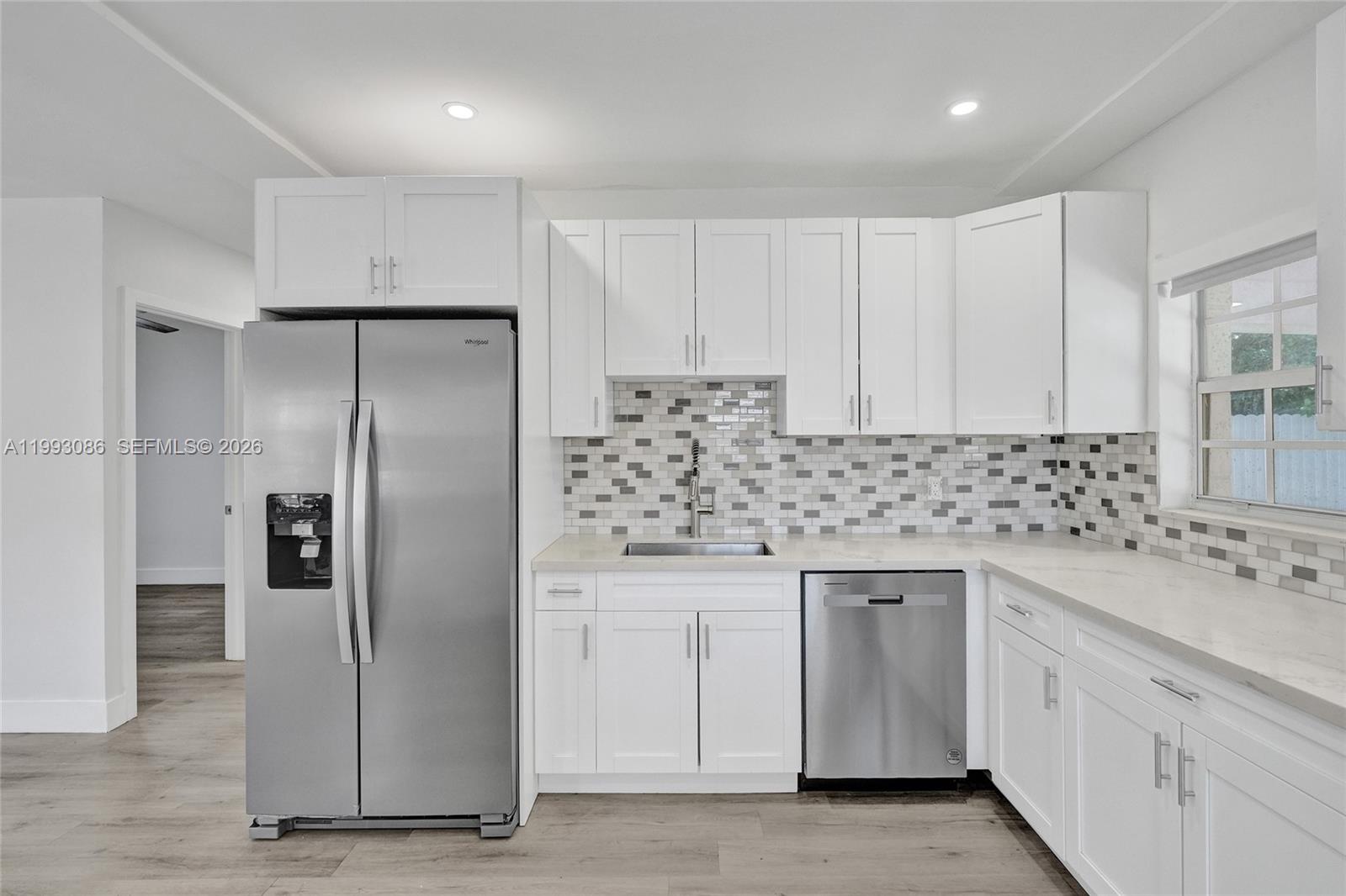 A kitchen features white cabinets, stainless steel appliances, a tiled backsplash, and light wood flooring — 4326 NW 4th St, Miami FL 33126, MIAMI, FL