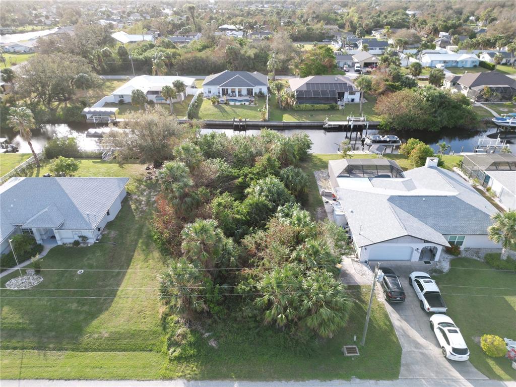 An aerial view shows a vacant, tree-covered lot situated between two residential houses and water — 4194 YUCATAN CIRCLE, PORT CHARLOTTE, FL