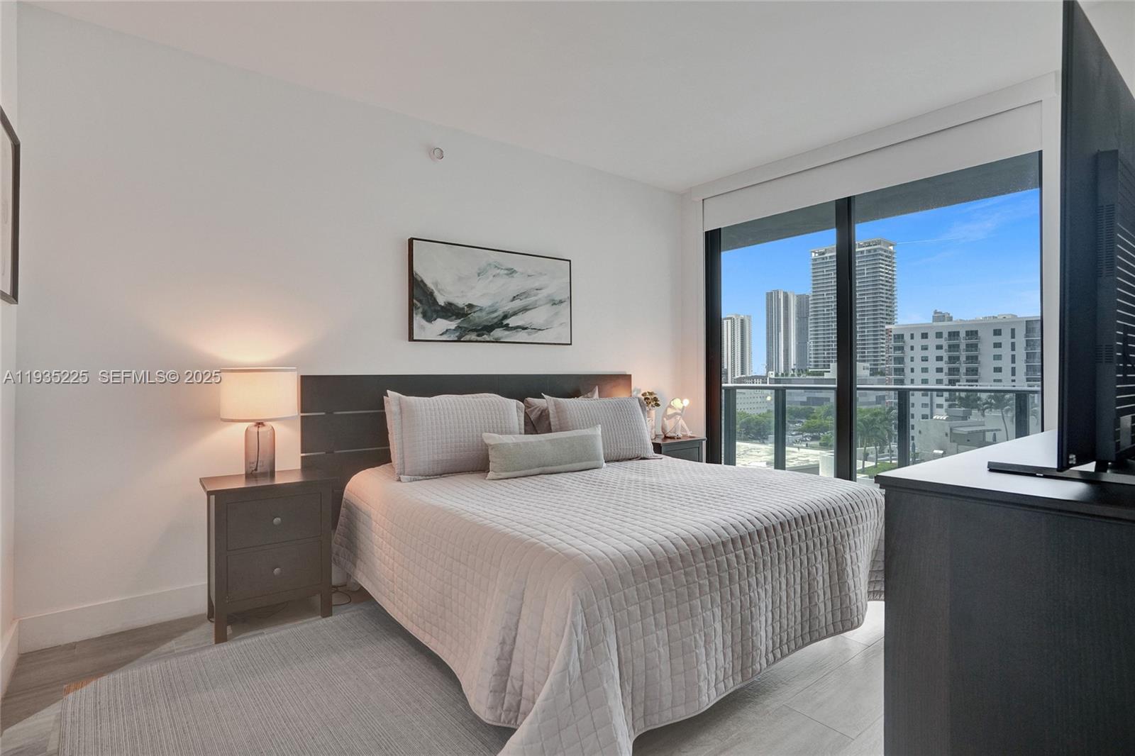A bedroom features a bed with a gray quilt, a dark headboard, and city views — 121 NE 34th St # 902, Miami FL 33137, MIAMI, FL
