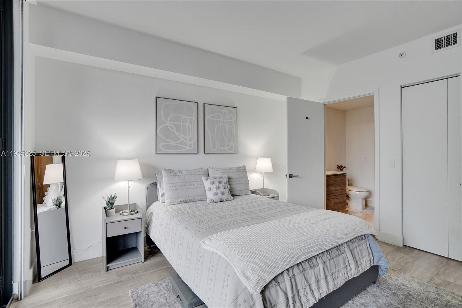 A bedroom features a bed with grey bedding, two nightstands with lamps, and an attached bathroom — 121 NE 34th St # 902, Miami FL 33137, MIAMI, FL