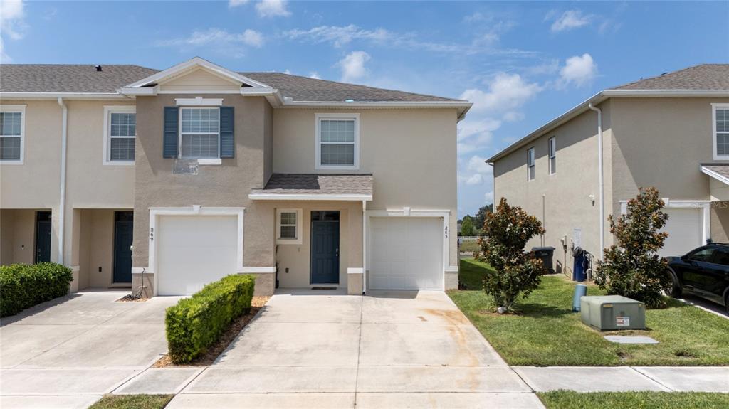 A two-story townhouse exterior features beige stucco walls, two garage doors, and a concrete driveway — 265 FELTRIM RESERVE BOULEVARD, DAVENPORT, FL