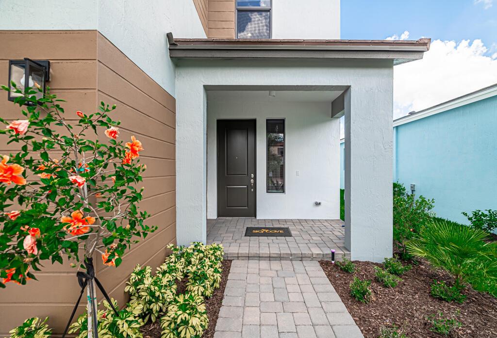 A paved walkway leads to the covered front entrance of a modern home with landscaping — 16469 Sea Turtle Place, Westlake FL 33470, WESTLAKE, FL