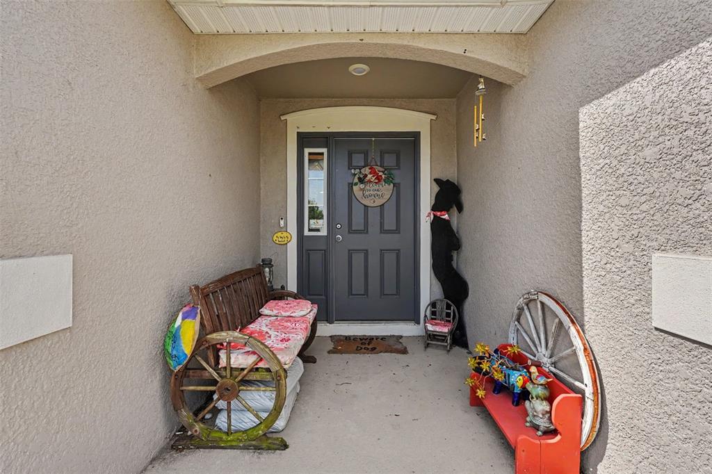A covered front porch features a wooden wagon-wheel bench, a red bench, and a gray door — 11820 STONE PINE STREET, RIVERVIEW, FL