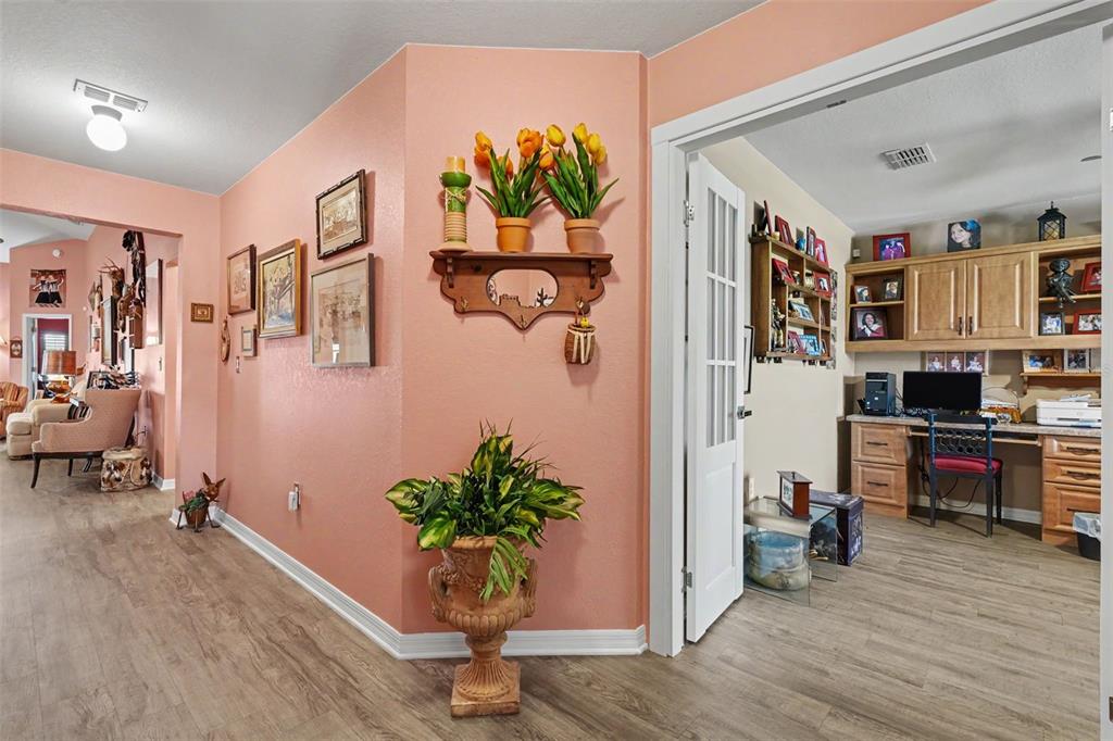 A peach-colored hallway leads to an office with wooden cabinets and a desk — 11820 STONE PINE STREET, RIVERVIEW, FL