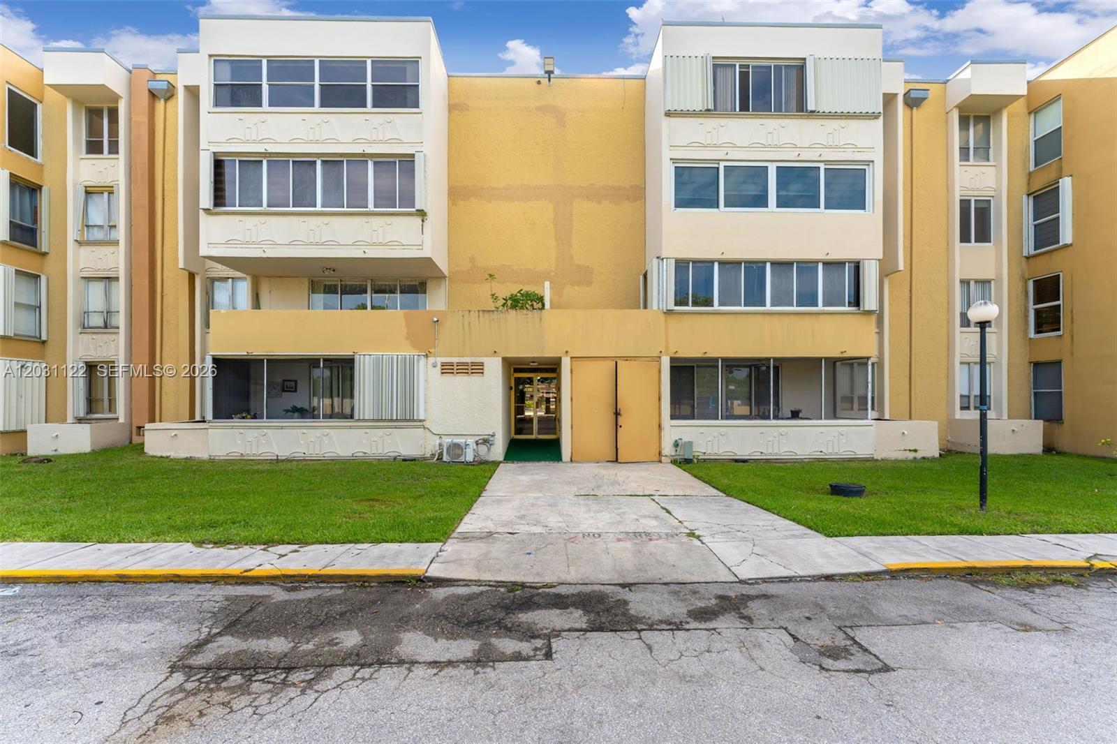 A three-story yellow apartment building with a central entrance and a concrete walkway — 6911 SW 147th Ave # 2H, Miami FL 33193, MIAMI, FL