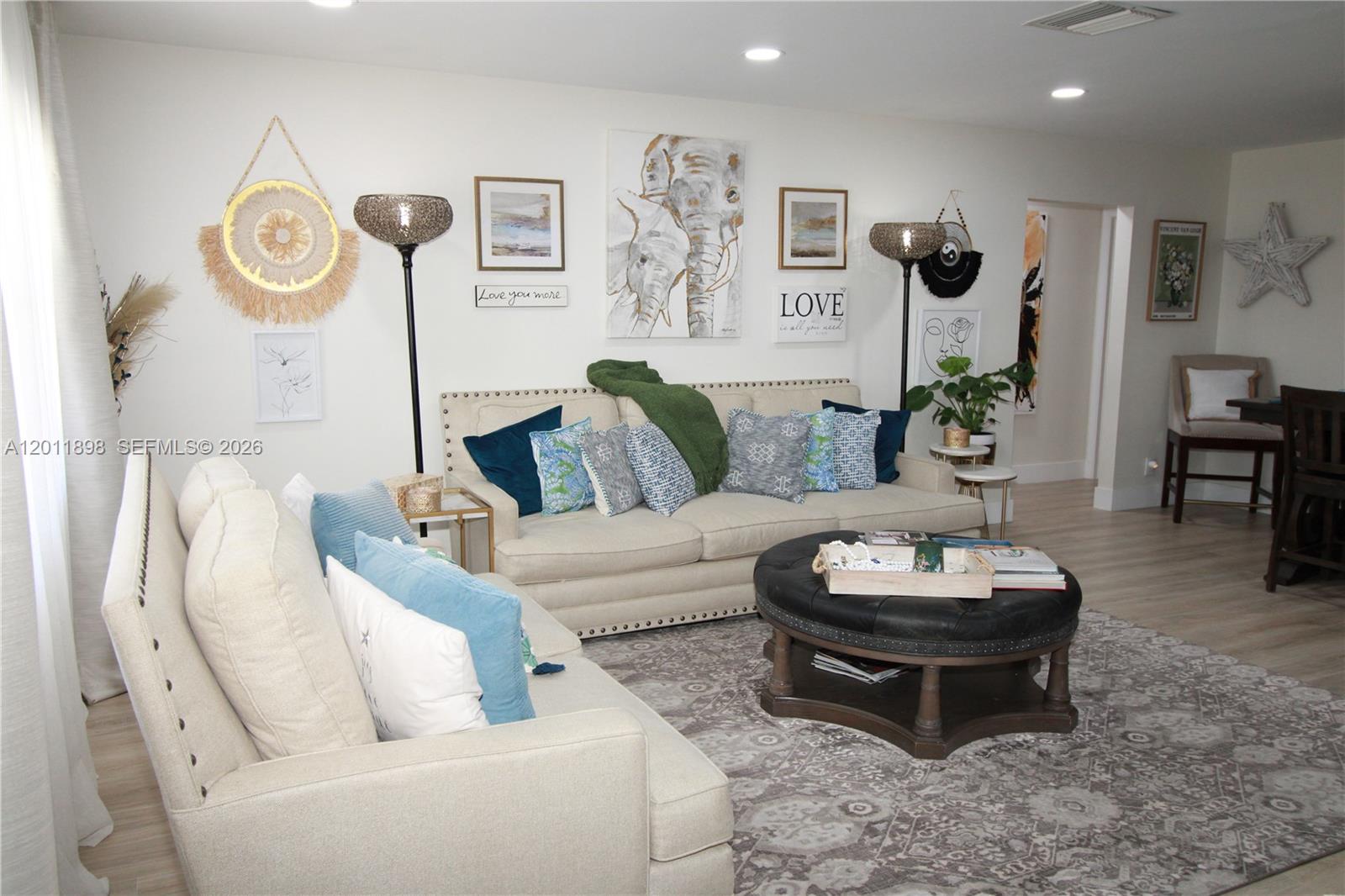 A living room features two beige sofas, a black round ottoman, and wall-mounted artwork — 1511 Alfred Dr, Boynton Beach FL 33426, BOYNTON BEACH, FL