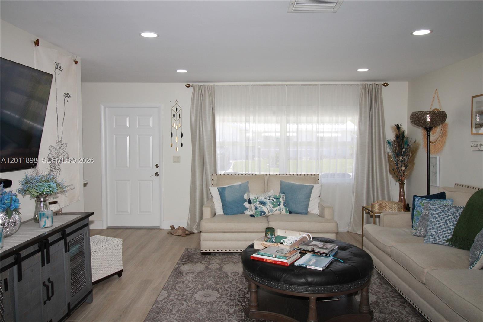 A living room features a beige sofa, a round leather ottoman, and light wood flooring — 1511 Alfred Dr, Boynton Beach FL 33426, BOYNTON BEACH, FL