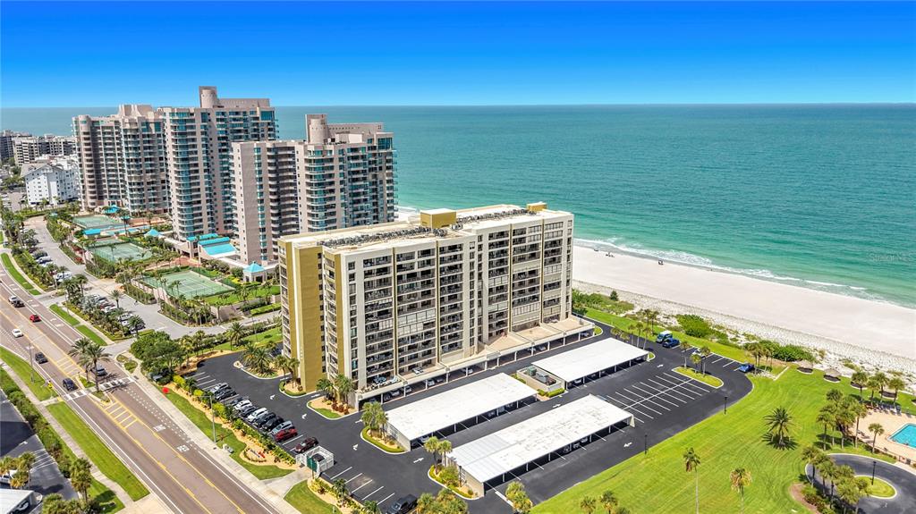 An aerial view shows a multi-story beachfront condominium complex with parking lots and tennis courts — 1480 GULF BOULEVARD UNIT 611, CLEARWATER, FL