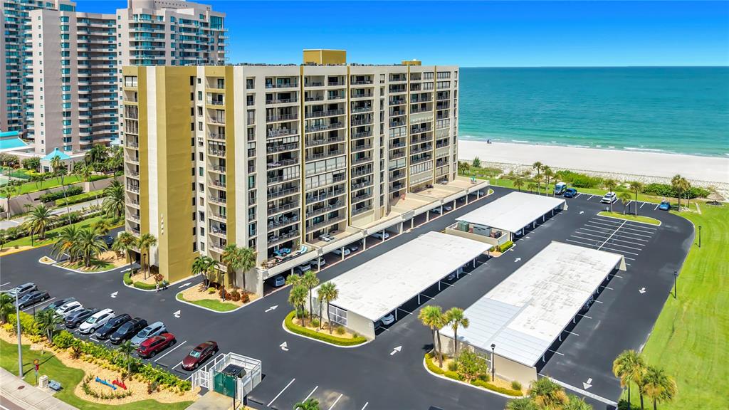 An aerial view shows a multi-story apartment building with a parking lot near the beach — 1480 GULF BOULEVARD UNIT 611, CLEARWATER, FL
