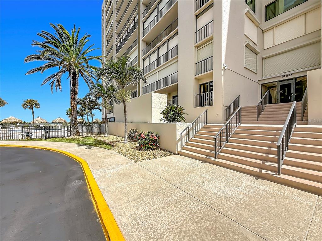 A concrete staircase leads to the entrance of a multi-story building with palm trees nearby — 1480 GULF BOULEVARD UNIT 611, CLEARWATER, FL