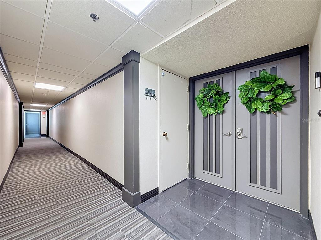 A hallway with striped carpet leads to a double door entrance featuring two green wreaths — 1480 GULF BOULEVARD UNIT 611, CLEARWATER, FL