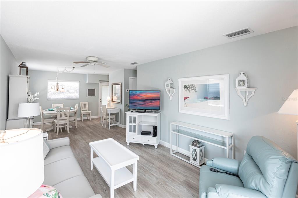A bright living and dining area features light-colored furniture, gray wood-look flooring, and coastal decor — 6020 MIDNIGHT PASS ROAD UNIT 11, SARASOTA, FL