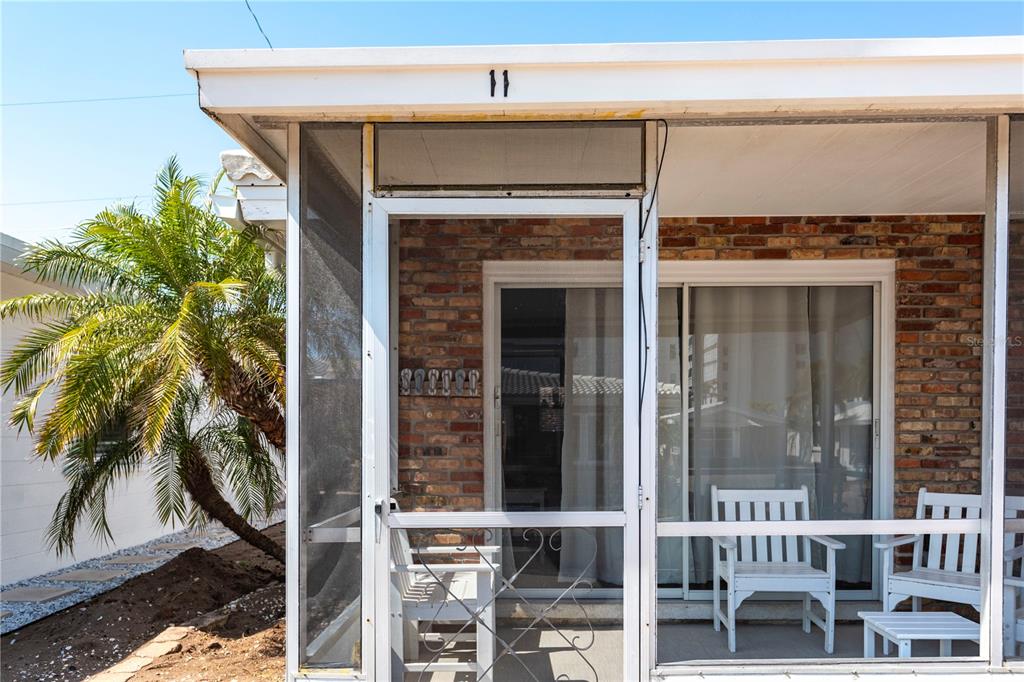 A screened-in porch with brick walls and white furniture sits under a roof overhang — 6020 MIDNIGHT PASS ROAD UNIT 11, SARASOTA, FL