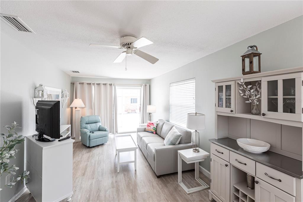 A living room features light wood-look flooring, a gray sofa, a blue recliner, and cabinetry — 6020 MIDNIGHT PASS ROAD UNIT 11, SARASOTA, FL