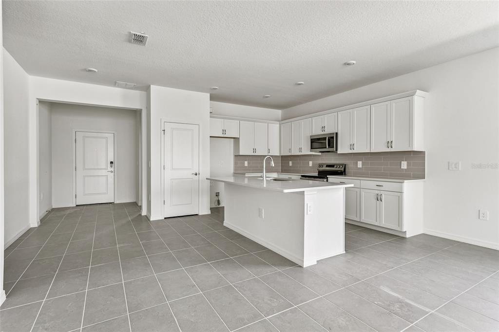 A modern kitchen features white cabinetry, a central island, and gray tile flooring — 9122 OPTIMIST WAY, PALMETTO, FL