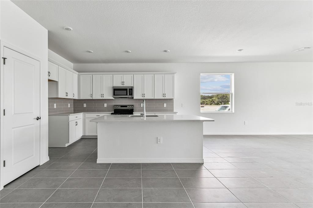 A modern kitchen features white cabinetry, a central island, gray tile flooring, and a window — 9122 OPTIMIST WAY, PALMETTO, FL
