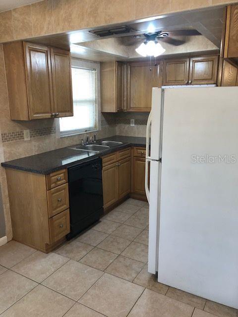A kitchen with wood cabinets, dark countertops, a white refrigerator, and tiled flooring — 10876 72ND AVENUE UNIT C, SEMINOLE, FL