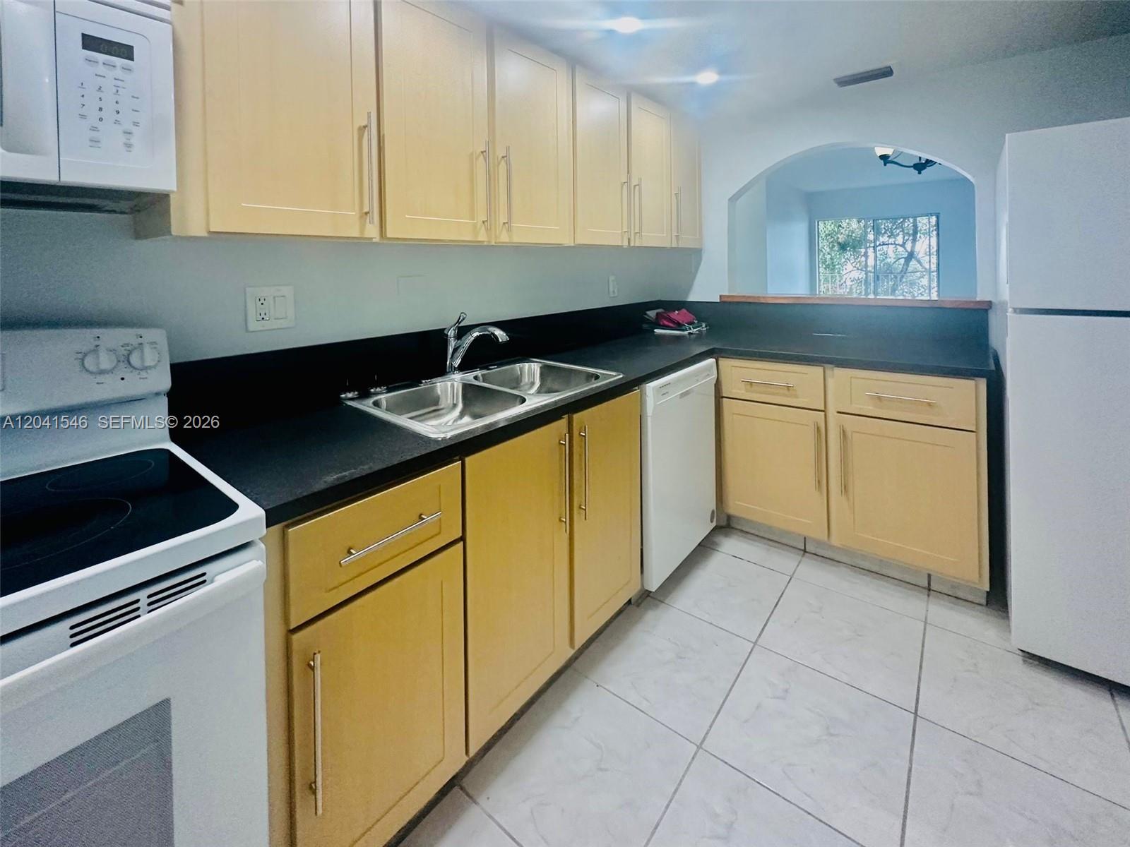 A kitchen features light wood cabinets, black countertops, white appliances, and a pass-through window — 8101 SW 73rd Ave # 09, Miami FL 33143, MIAMI, FL