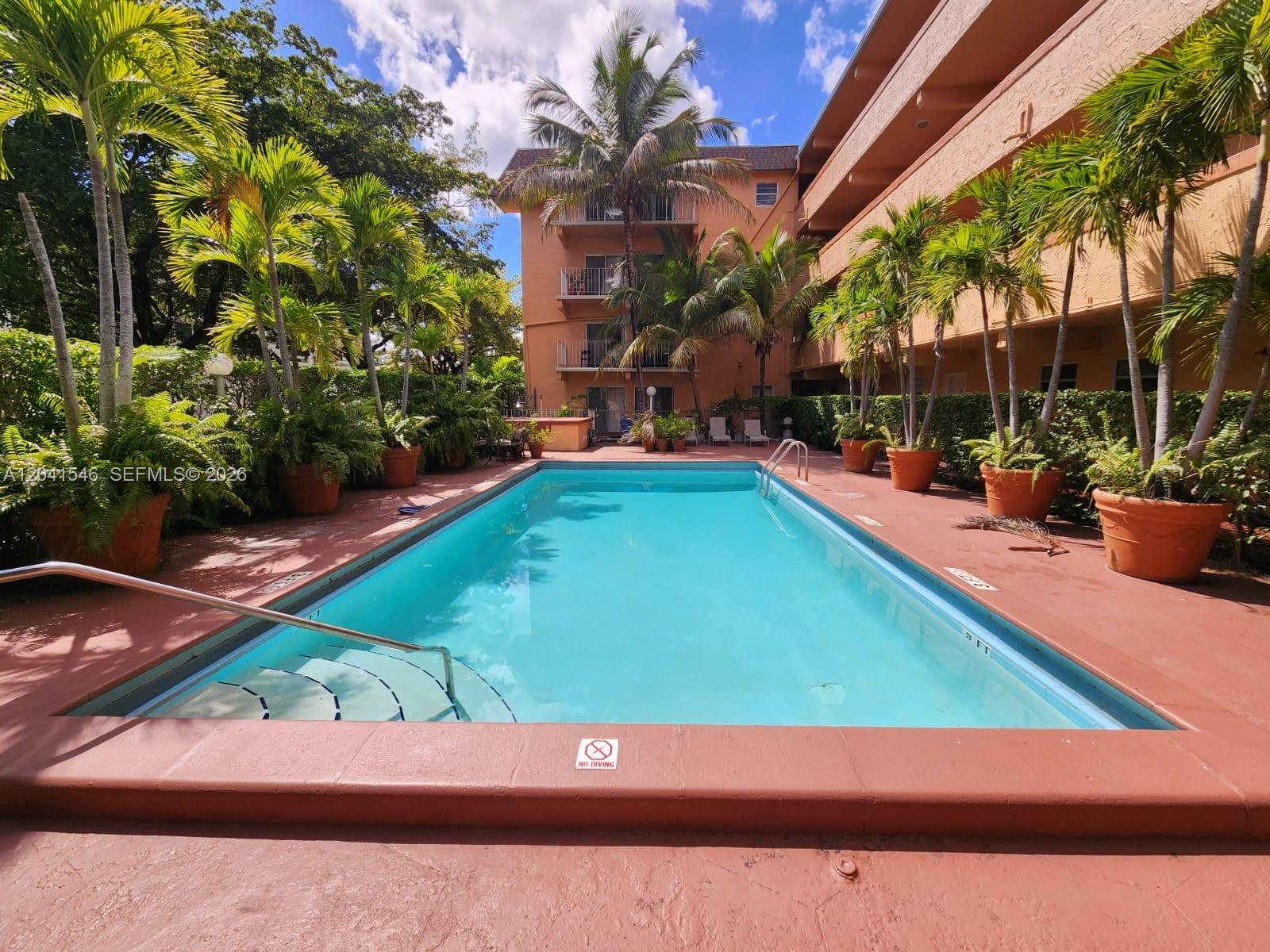 An outdoor swimming pool is surrounded by potted palm trees and a multi-story apartment building — 8101 SW 73rd Ave # 09, Miami FL 33143, MIAMI, FL