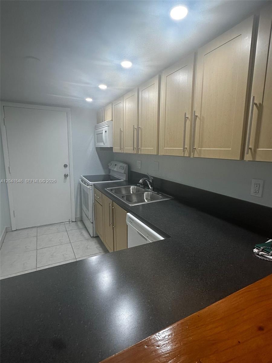 A galley kitchen features light wood cabinets, dark countertops, and a white appliance suite — 8101 SW 73rd Ave # 09, Miami FL 33143, MIAMI, FL