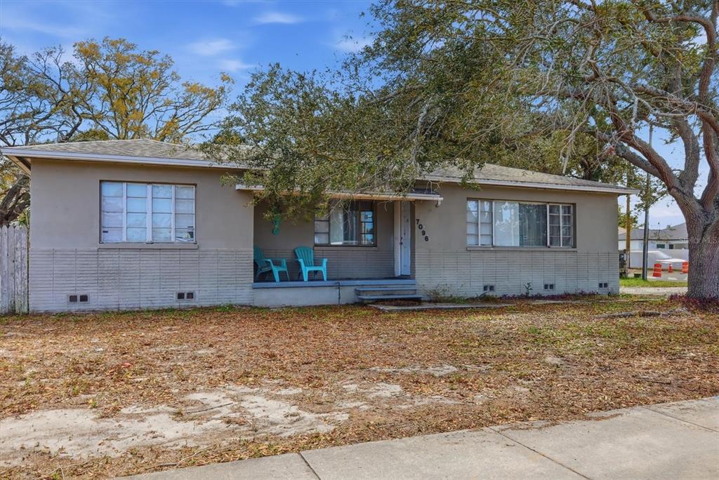 A single-story house with a covered porch, two blue chairs, and a large oak tree — 7096 54TH AVENUE N, ST PETERSBURG, FL