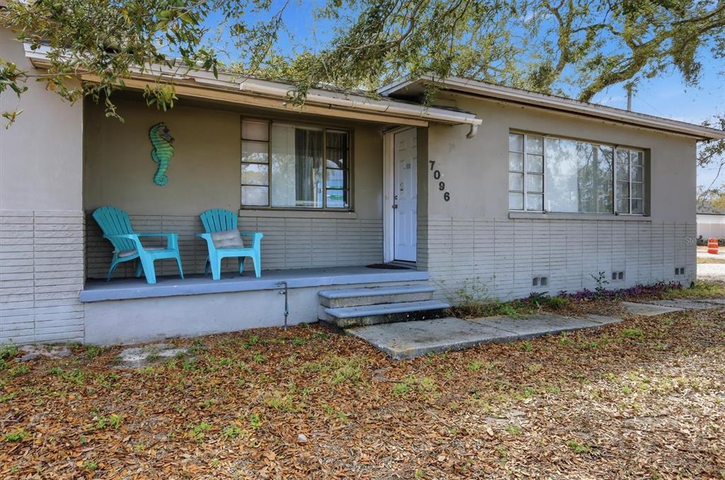 A single-story house with a covered porch, two blue chairs, and a light-colored exterior — 7096 54TH AVENUE N, ST PETERSBURG, FL
