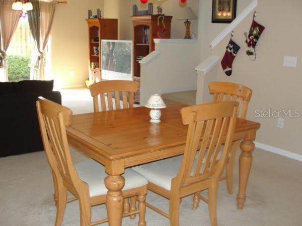 A wooden dining table with four chairs sits in a carpeted room near a staircase — 2537 HARN BOULEVARD UNIT 1, CLEARWATER, FL