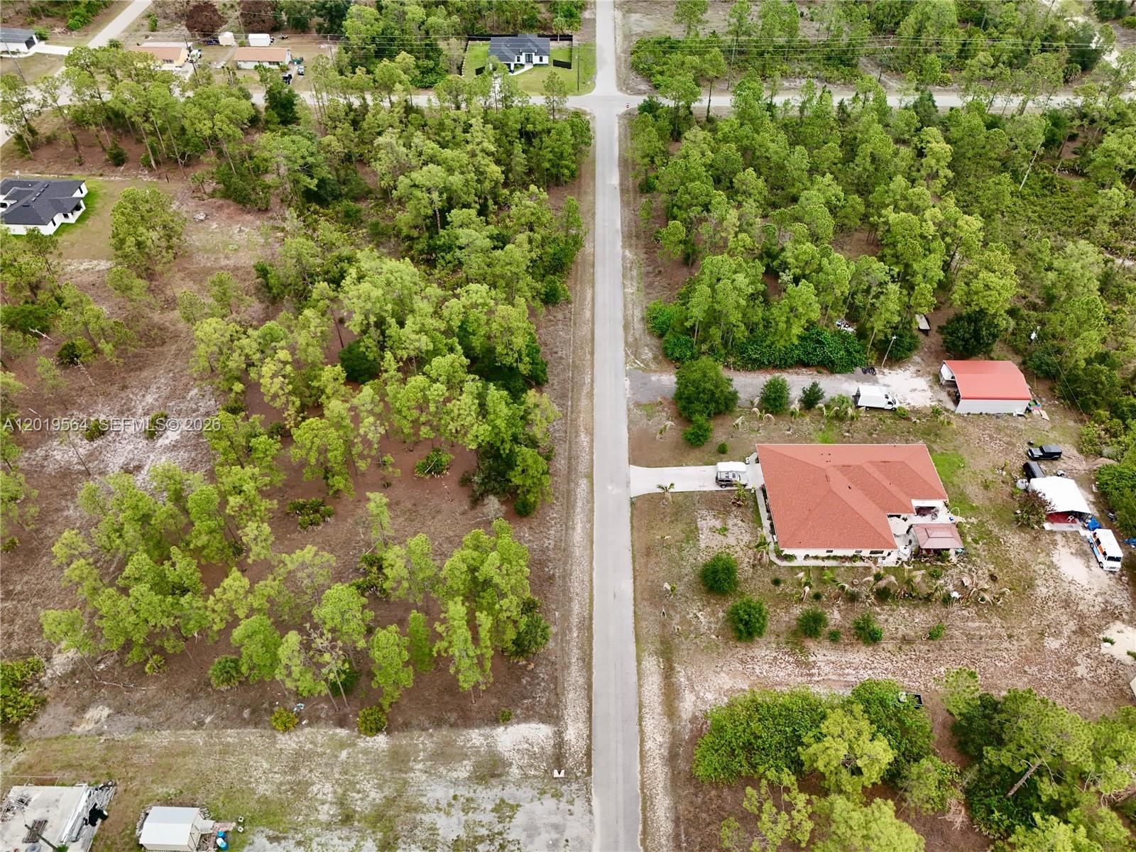 An aerial view shows a paved road running between a wooded lot and a residential property — 1417 Thompson Ave, Lehigh Acres FL 33972, LEHIGH ACRES, FL