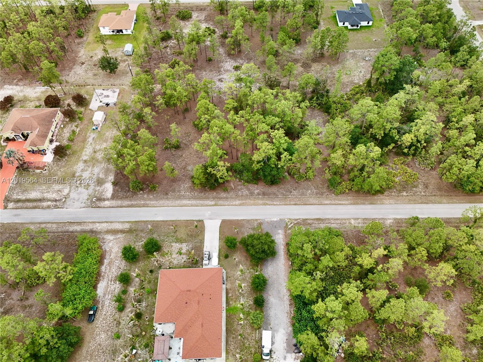 An aerial view shows several houses surrounded by wooded lots and a paved road — 1417 Thompson Ave, Lehigh Acres FL 33972, LEHIGH ACRES, FL