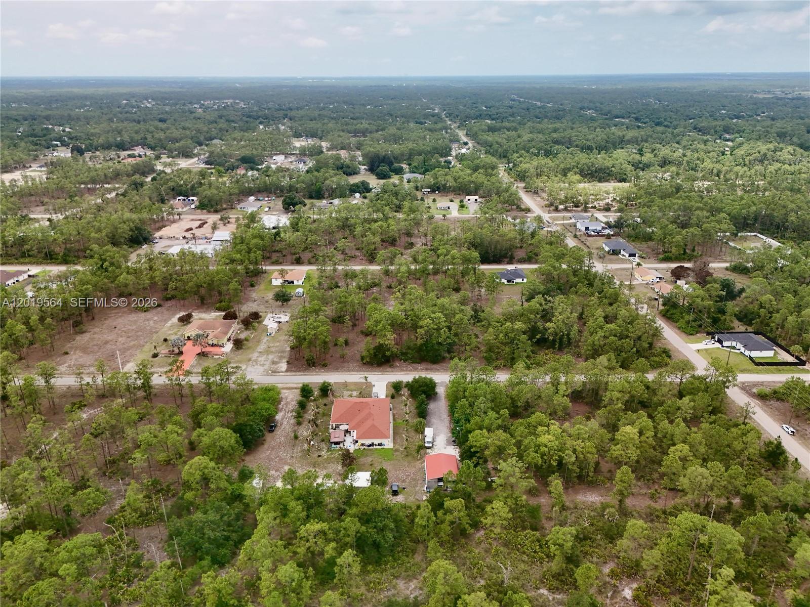 An aerial view shows several houses scattered among dense trees and dirt roads — 1417 Thompson Ave, Lehigh Acres FL 33972, LEHIGH ACRES, FL