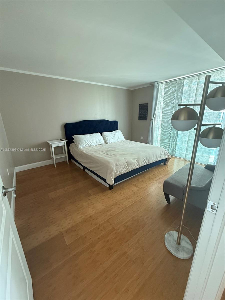 A bedroom features a blue upholstered bed, light wood flooring, and a floor lamp — 2101 Brickell Ave # 508, Miami FL 33129, MIAMI, FL