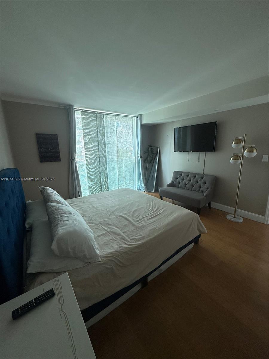 A bedroom features a blue tufted headboard, a gray loveseat, and a wall-mounted television — 2101 Brickell Ave # 508, Miami FL 33129, MIAMI, FL