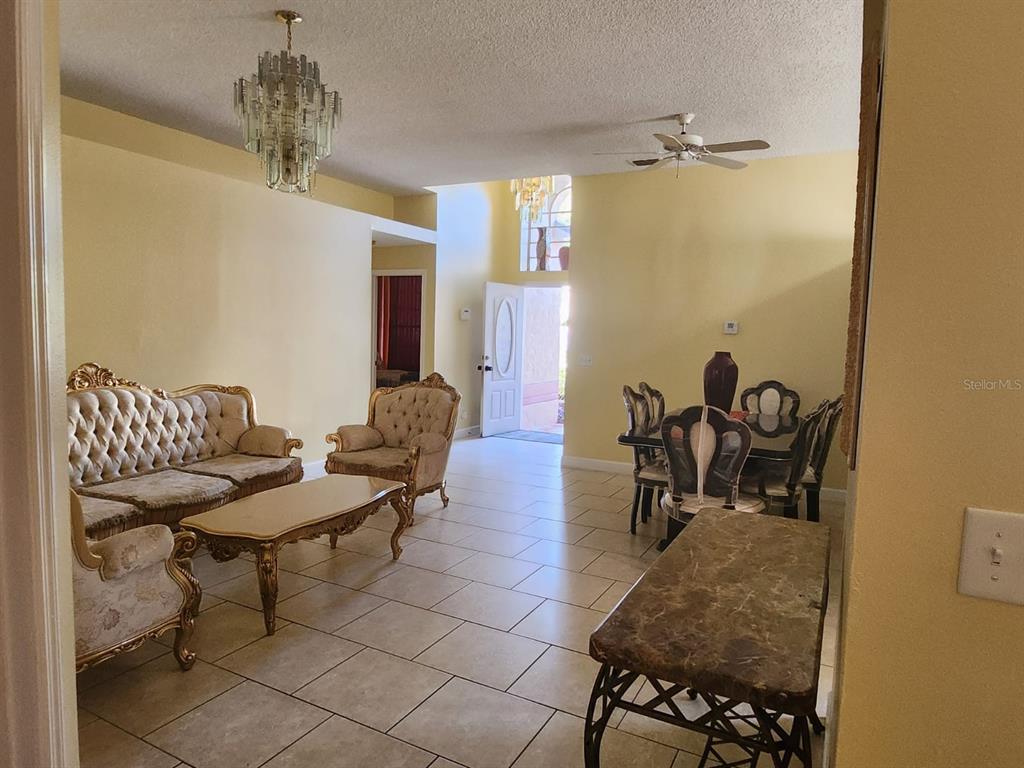 A living and dining area with tile floors, ornate furniture, and a crystal chandelier — 12210 HATFIELD COURT, ORLANDO, FL