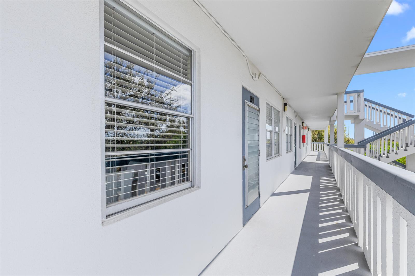 An exterior walkway with white walls, a window, a door, and a staircase — 3028 Harwood D, Deerfield Beach FL 33442, DEERFIELD BEACH, FL