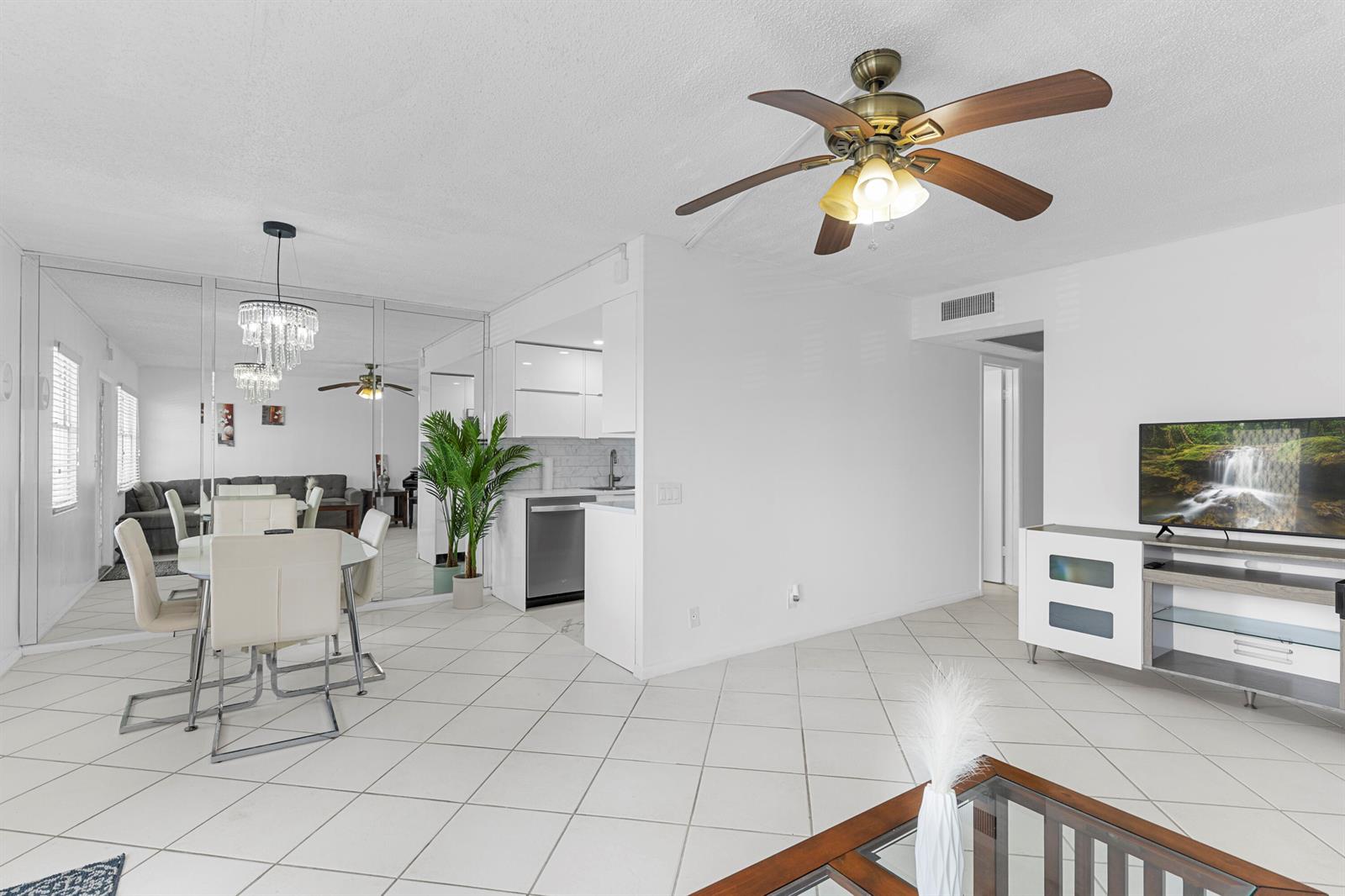 A bright living and dining area features white tile floors, a ceiling fan, and mirrors — 3028 Harwood D, Deerfield Beach FL 33442, DEERFIELD BEACH, FL
