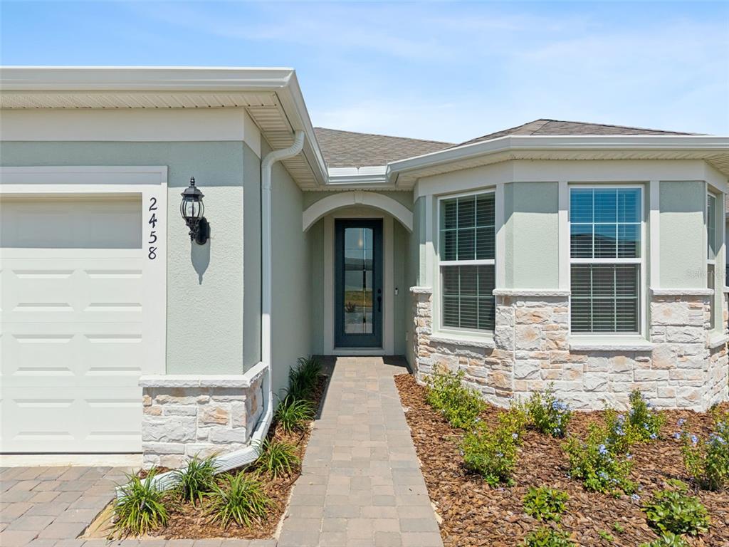 The exterior of a house features a stone-accented facade, a paved walkway, and a garage — 2458 DEL WEBB DRIVE, MINNEOLA, FL