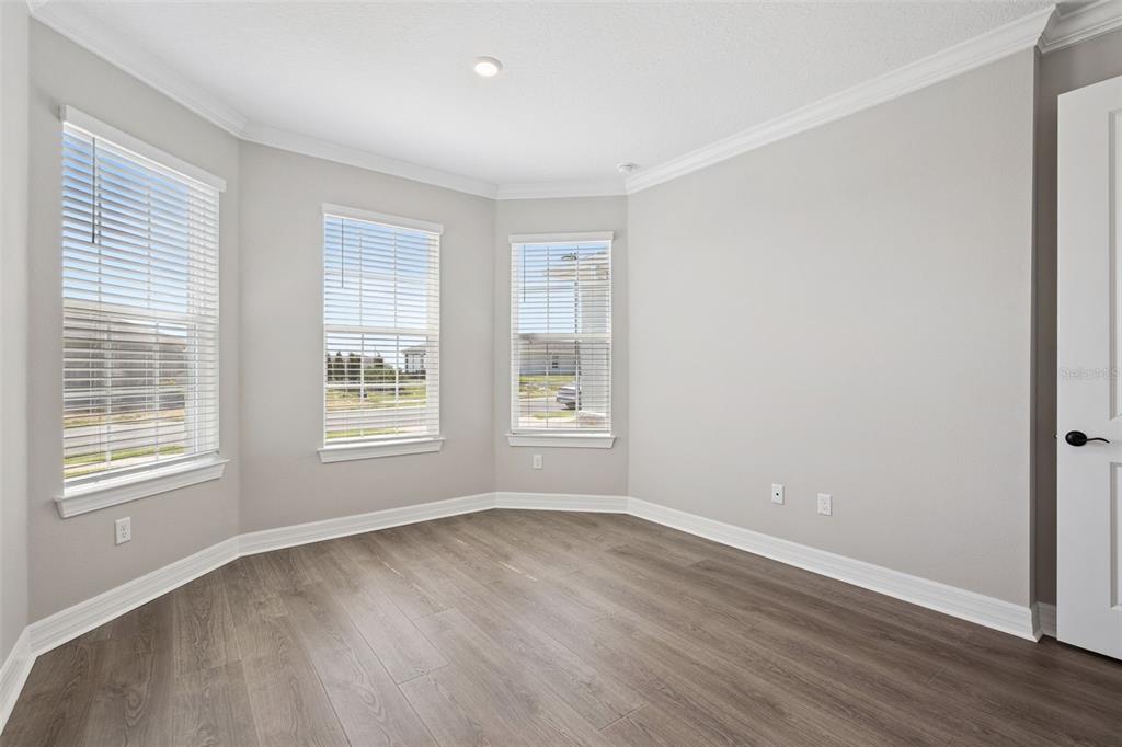 An empty room with gray walls, wood-look flooring, crown molding, and three large windows — 2458 DEL WEBB DRIVE, MINNEOLA, FL