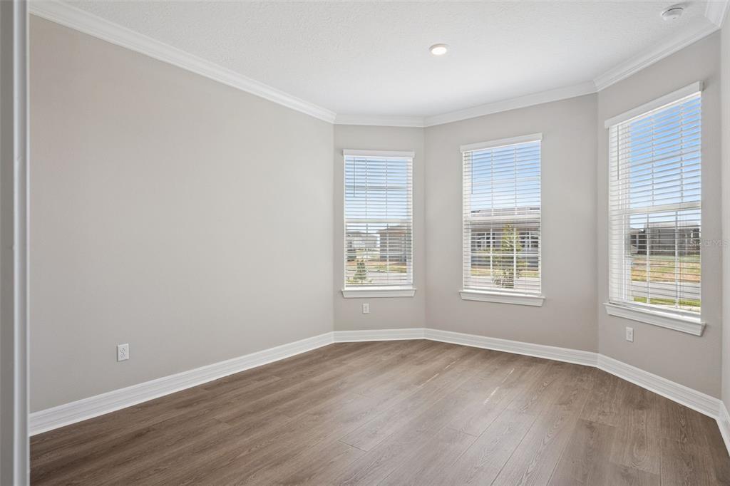 An empty room with light gray walls, wood-look flooring, and three windows in a bay configuration — 2458 DEL WEBB DRIVE, MINNEOLA, FL
