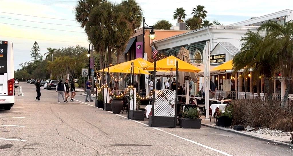 An outdoor restaurant patio features yellow umbrellas and tables along a street with palm trees — 40 S BLVD OF THE PRESIDENTS, SARASOTA, FL