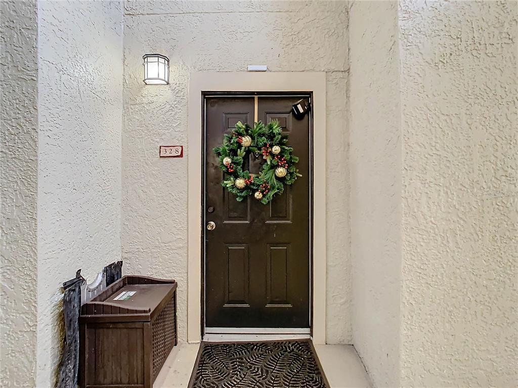 A dark brown front door with a holiday wreath is set in a stucco entryway — 114 VISTA VERDI CIRCLE UNIT 328, LAKE MARY, FL
