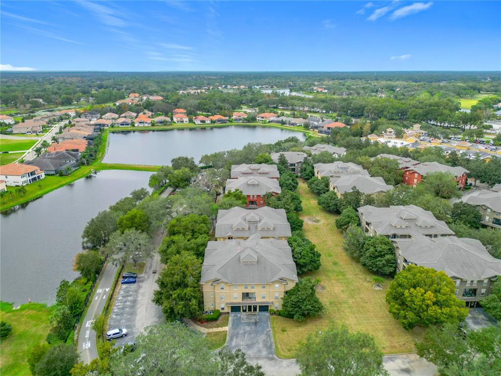 An aerial view shows apartment buildings situated next to a lake in a suburban area — 114 VISTA VERDI CIRCLE UNIT 328, LAKE MARY, FL