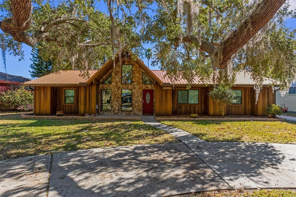 A single-story house with wood siding, a metal roof, and a stone-accented front entrance — 11870 W RIVERHAVEN DRIVE, HOMOSASSA, FL