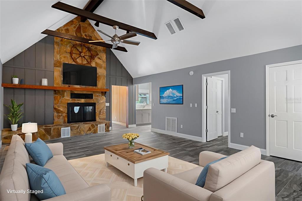 A living room features a stone fireplace, vaulted ceilings with exposed beams, and gray flooring — 11870 W RIVERHAVEN DRIVE, HOMOSASSA, FL