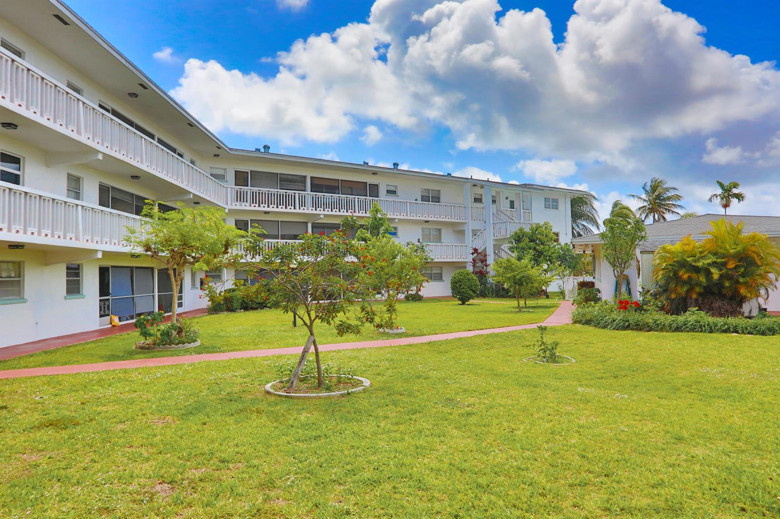 A multi-story apartment building with white balconies overlooks a grassy courtyard with trees — 600 Pine Drive # 209, Pompano Beach FL 33060, POMPANO BEACH, FL